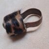A ring featuring a metallic band with an embossed scroll pattern and a top section covered in brown and black leopard print fur. The metal has a dark, aged finish, and the fur texture is visible across the rounded top surface. — Khodamdjin