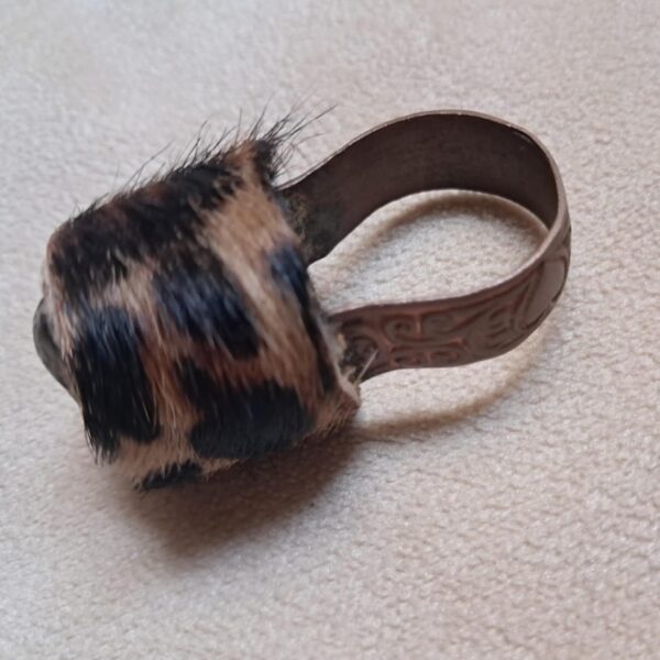 A ring featuring a metallic band with an embossed scroll pattern and a top section covered in brown and black leopard print fur. The metal has a dark, aged finish, and the fur texture is visible across the rounded top surface. — Khodamdjin