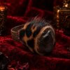 A ring featuring a dark, smooth, rounded stone centerpiece surrounded by a textured, brown and black animal print fur trim. The metal band is silver-toned and decorated with an intricate, embossed scrollwork pattern along its outer surface. — Khodamdjin