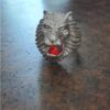 A silver-toned metal ring featuring a sculpted lion head design with a prominent mane. The lion's open mouth contains a single, faceted, bright red gemstone set within the center, creating a striking contrast against the metallic finish. — Khodamdjin