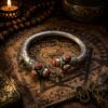 A silver-toned metal cuff bracelet featuring an open design with textured bands and decorative end caps. Each end is adorned with three embedded, round, reddish-brown glittery stones that have a sparkling, speckled appearance. — Khodamdjin