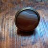 A round ring featuring a polished, banded agate gemstone with horizontal layers of brown, tan, and white. The stone is set within a smooth, metallic bezel that encircles the circumference of the cabochon, highlighting the natural, earthy color variations of the stone. — Khodamdjin