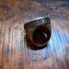 A metallic ring featuring an engraved band with Arabic calligraphy text that reads Qul Huwa Allahu Ahad. The ring has a dark, oxidized finish with intricate scrollwork patterns along the sides and a smooth, rounded inner band. — Khodamdjin