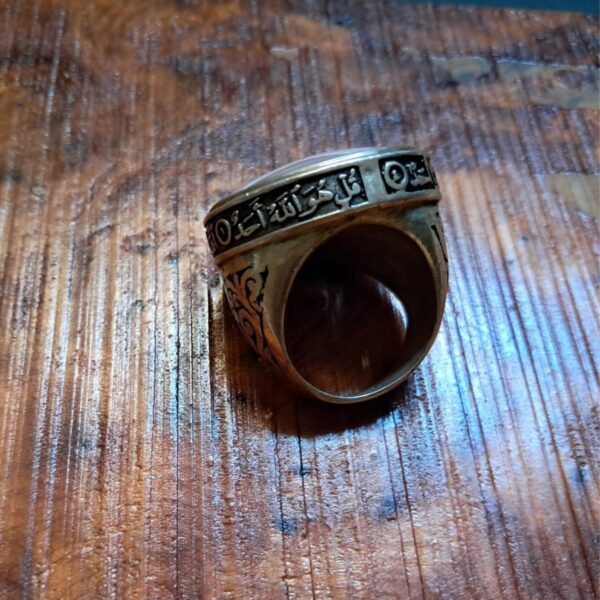 A metallic ring featuring an engraved band with Arabic calligraphy text that reads Qul Huwa Allahu Ahad. The ring has a dark, oxidized finish with intricate scrollwork patterns along the sides and a smooth, rounded inner band. — Khodamdjin