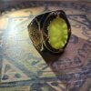 A silver ring with gold accents and a large, oval, yellow gemstone. The ring has intricate filigree designs on the sides and around the gemstone. The setting is dark, contrasting with the bright stone. — Khodamdjin