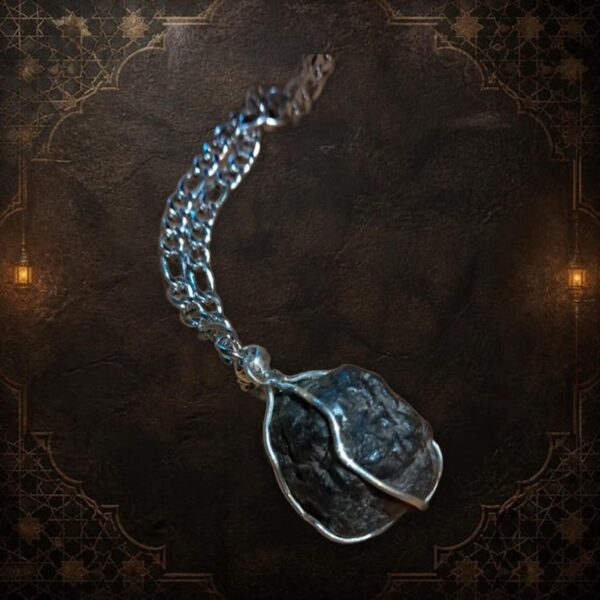A necklace featuring a dark, rough, irregularly shaped stone pendant encased in a silver-colored wire wrap. The pendant is suspended from a silver-colored metal chain with oval-shaped links, creating a simple and functional piece of jewelry. — Khodamdjin