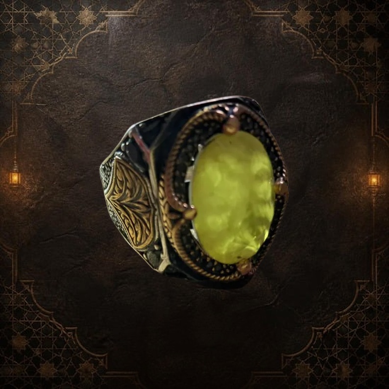 A silver ring with gold accents and a large, oval, yellow gemstone. The ring has intricate filigree designs on the sides and around the gemstone. The setting is dark, contrasting with the bright stone. — Khodamdjin