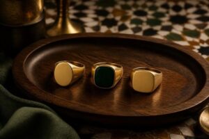 Three blank signet rings with oval, square and cushion faces arranged on dark walnut